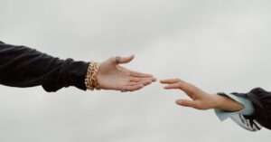 Close-up of two hands reaching for each other under a cloudy sky, symbolizing connection.