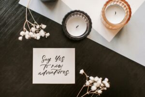Flat lay of a motivational note with candles and flowers on a wooden surface.